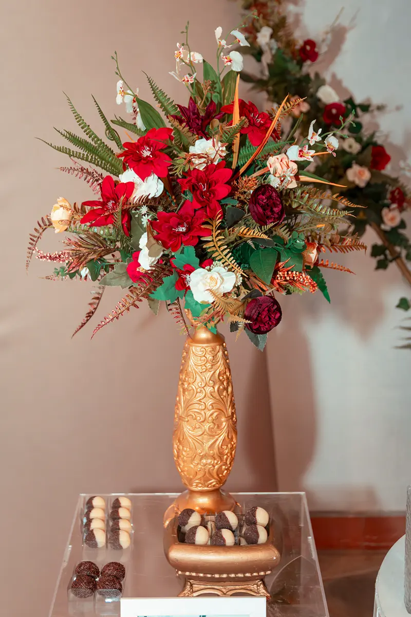 Arranjo de flores vermelhas e folhagem dourada num vaso dourado